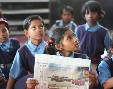 Schoolchildren in classroom reading a newspaper